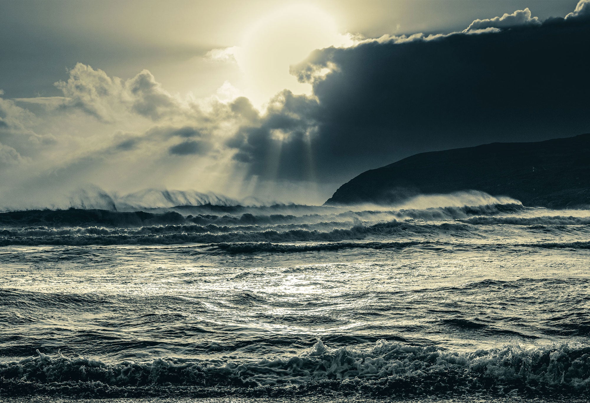 Stormy ocean with waves crashing against a cliff under a dramatic sky.
