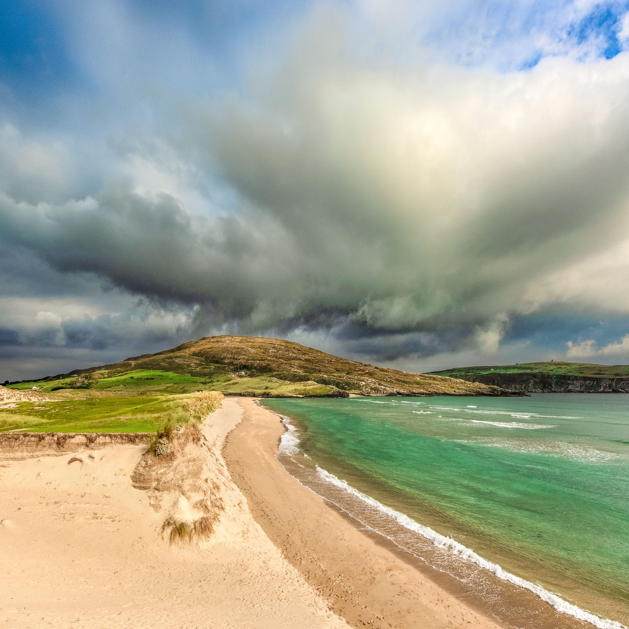 Beach with green water and a large cloud formation above