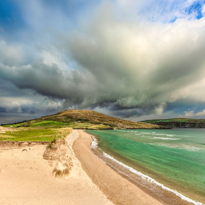 Beach with green water and a large cloud formation above