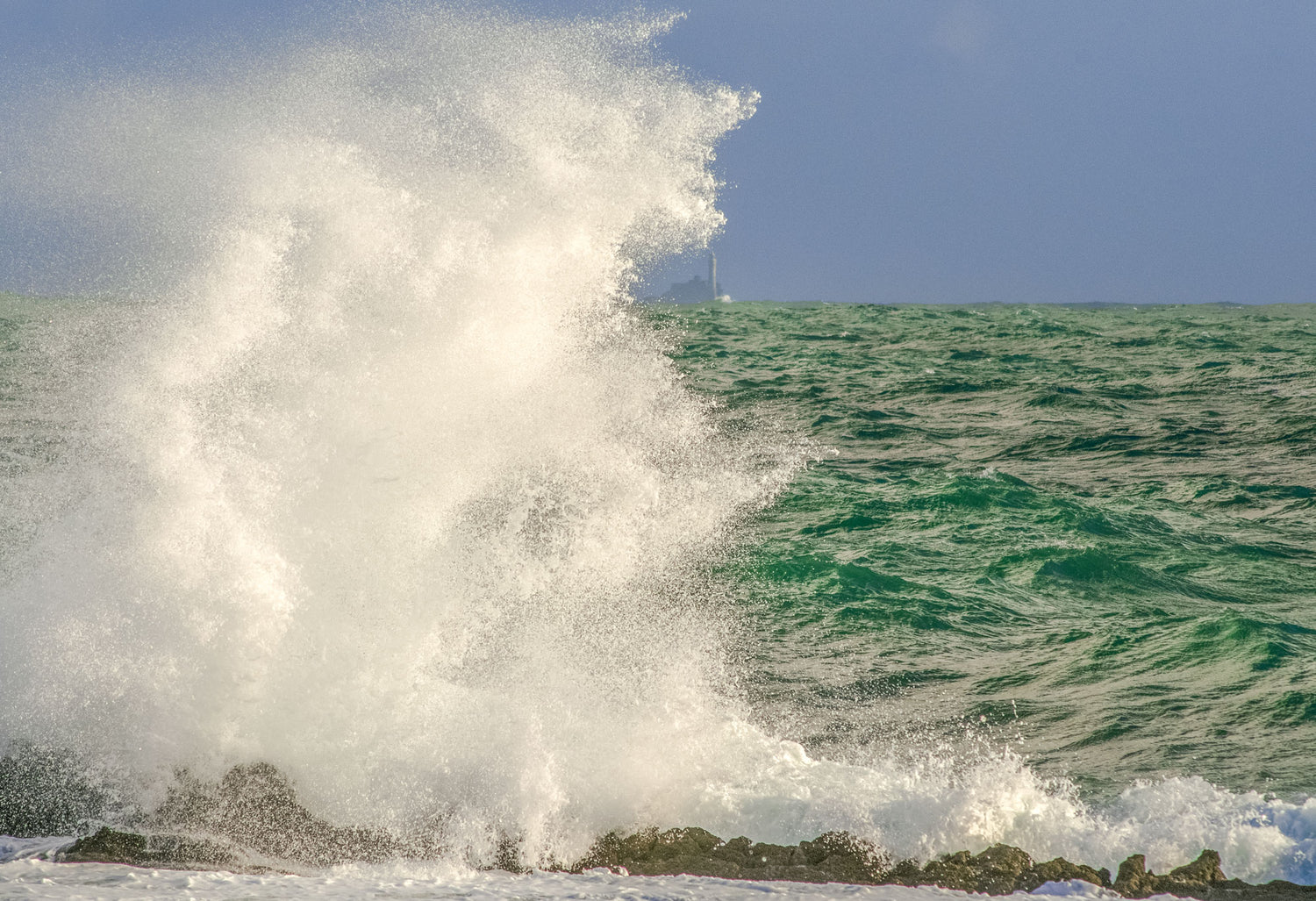 Wave crashing on rocks with a clear sky background