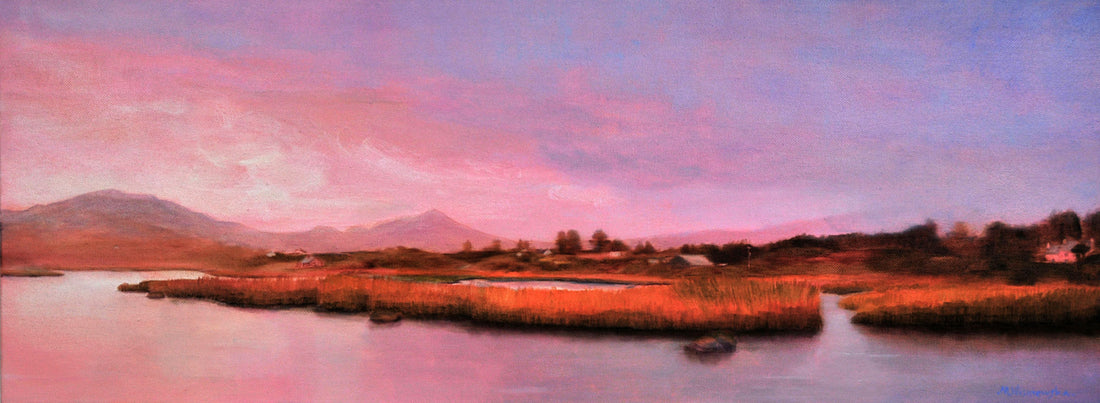 Panoramic landscape of a lake with reeds and mountains under a pink sky.